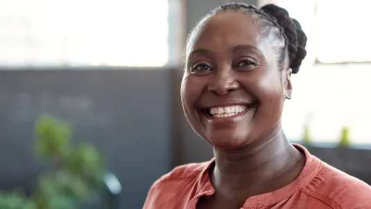 Portrait of a casually dressed young African businesswoman smiling confidently while standing alone in a bright modern office