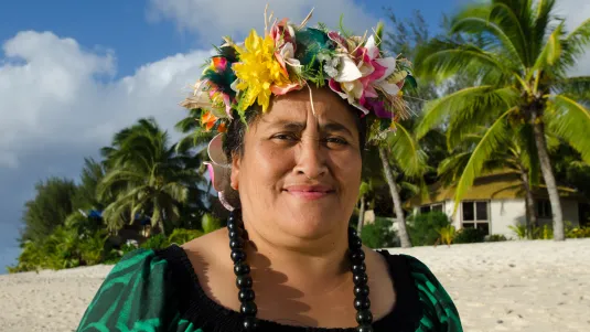 Portrait of active senior Polynesian Pacific Islander woman looking at the camera standing on tropical island beach with palm trees in the background in Rarotonga, Cook Islands