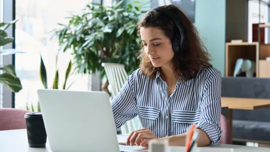 Latin hispanic girl college student wearing headphones taking online training class on laptop computer sitting at university table. Virtual education webinar, remote study, distance academic learning