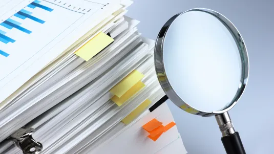 Investigate and analyze. Scanning business documents. Magnifying glass and stack of documents.