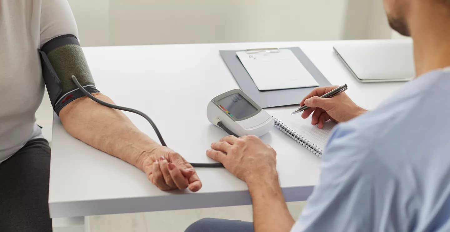Doctor at clinic checking arterial pressure of older woman. Senior lady diagnosed with hypertension gets blood pressure measured with tonometer during health checkup appointment visit to hospital