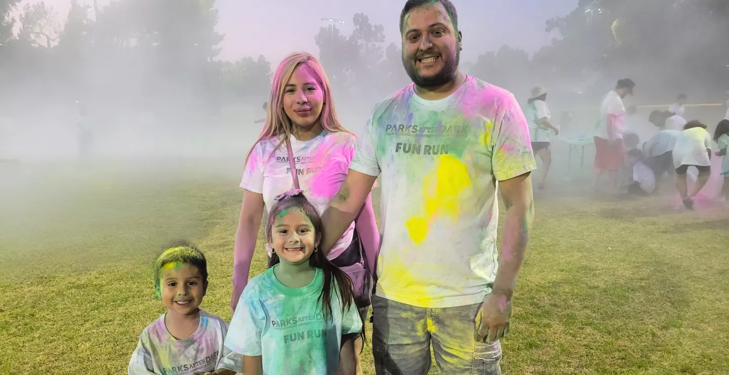 family wearing Parks After Dark t-shirts in park covered in powder paint