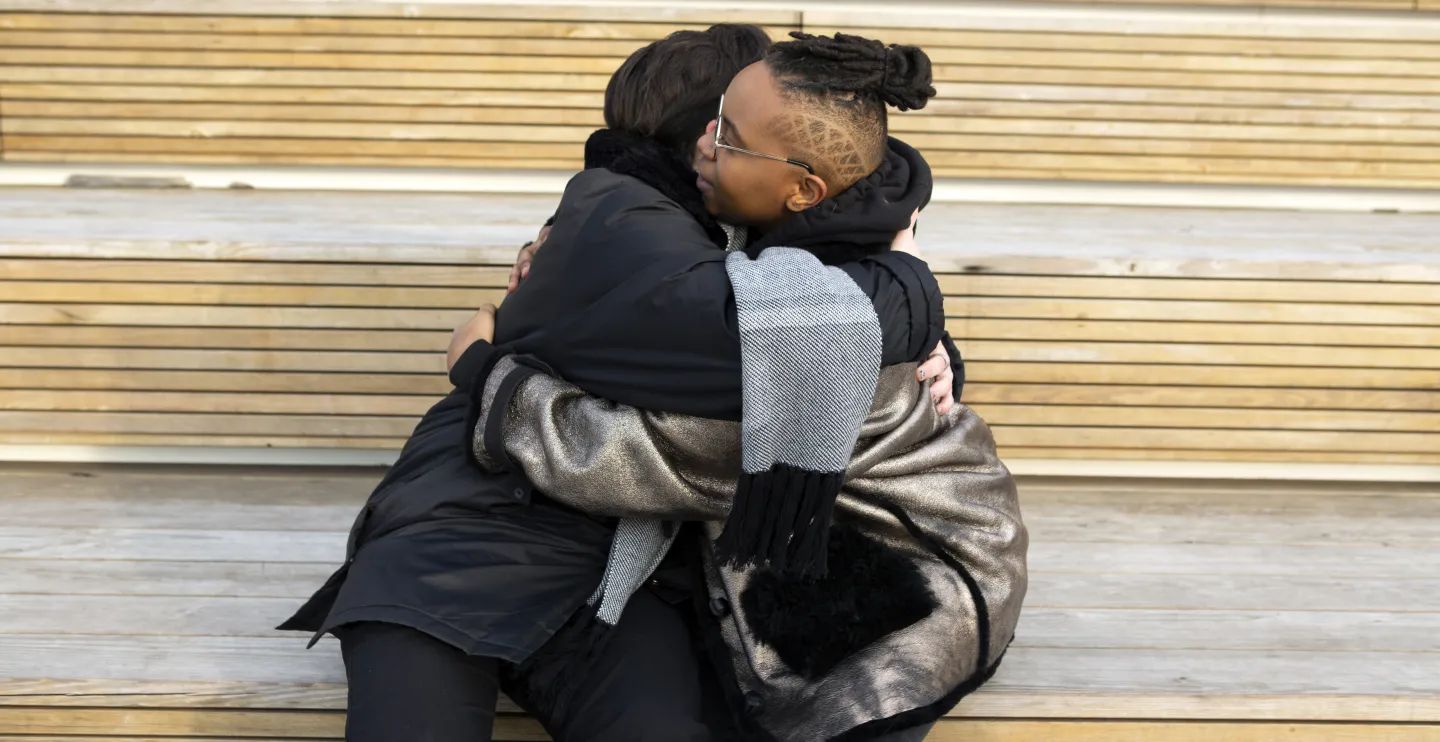 Two transmasculine friends embracing while sitting down