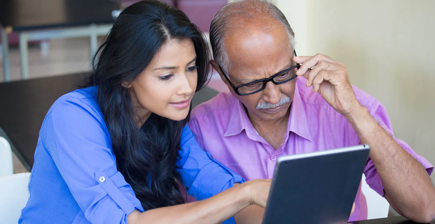 Woman helps a man older than her read information on a tablet computer.