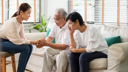 Photo of older Asian couple and younger Asian woman sitting in living room