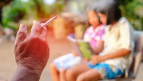 person smoking a cigarette next to children reading a book in a park