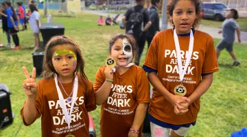 Three children wearing brown T-shirts that read Parks After Dark