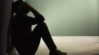 Photo of person in shadows, sitting with back against wall