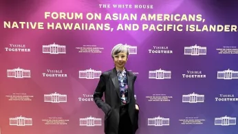 Ninez Ponce standing in front of a banner that says The White House Forum on Asian Americans, Native Hawaiians, and Pacific Islanders