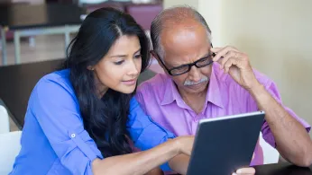 Woman helps a man older than her read information on a tablet computer.